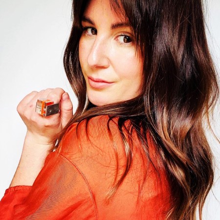 model wearing orange top looking over her shoulder and wearing clear Hebbe ring with neon orange insert, close to her face
